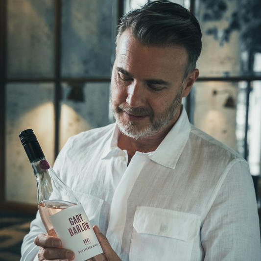 Gary Barlow admiring a bottle of his Sauvignon Blush wine in an elegant setting, showcasing his dedication to quality and craftsmanship.