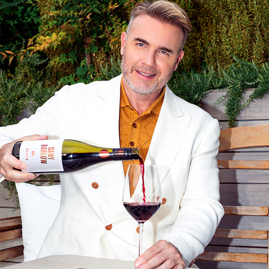 Gary Barlow pouring a glass of Malbec, a 750ml bottle with 12% ABV. Showcasing the rich and velvety red wine in an elegant outdoor setting.