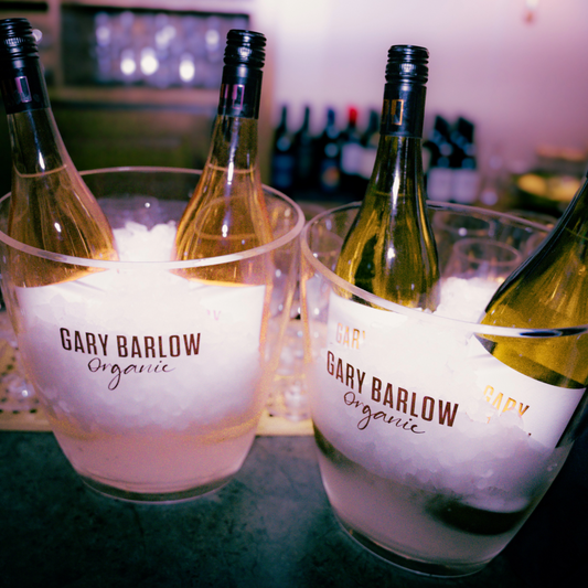 Chilled bottles of Gary Barlow Wine in branded ice buckets, filled with crushed ice, set on a bar counter with additional bottles in the background.